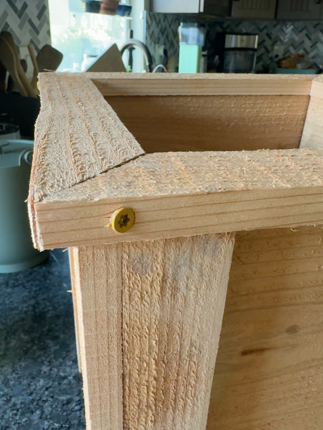 Close view of unfinished cedar trim, rough grain and a visible screw at a planter corner