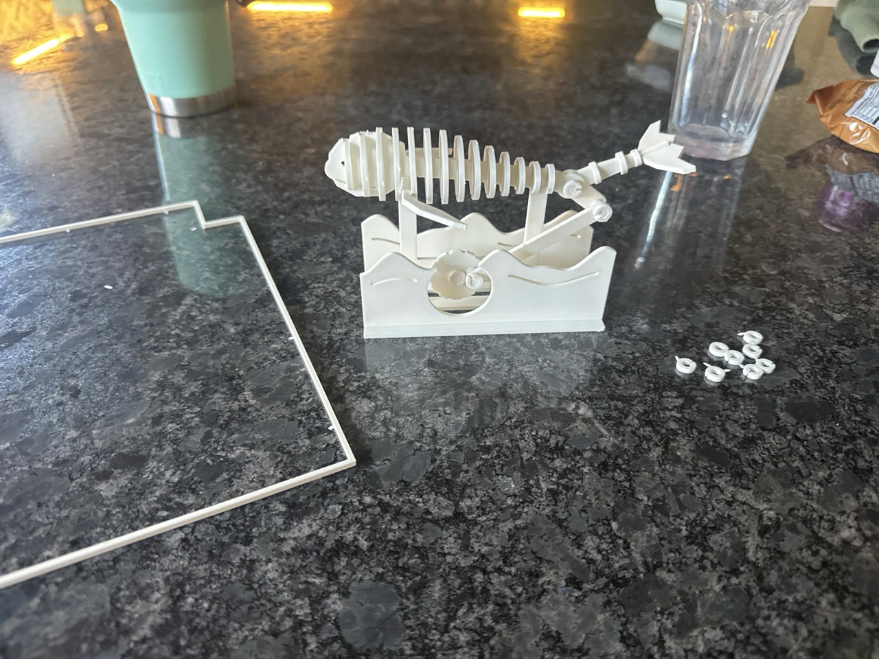 White mechanical whale assembled on a tabletop beside its empty kit frame and loose washers