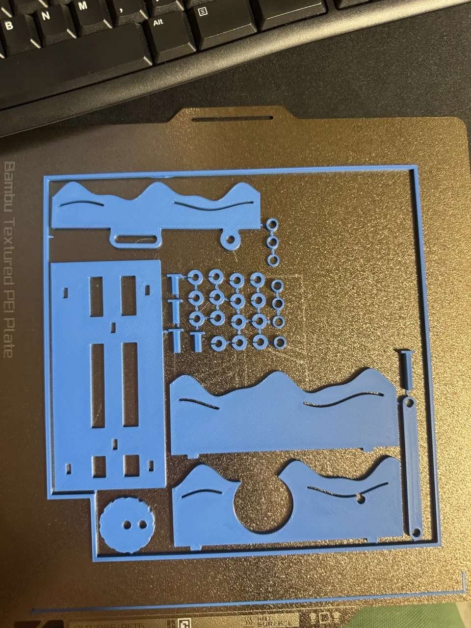 Blue 3D-printed wave base parts and small mechanical connectors on a printer build plate.