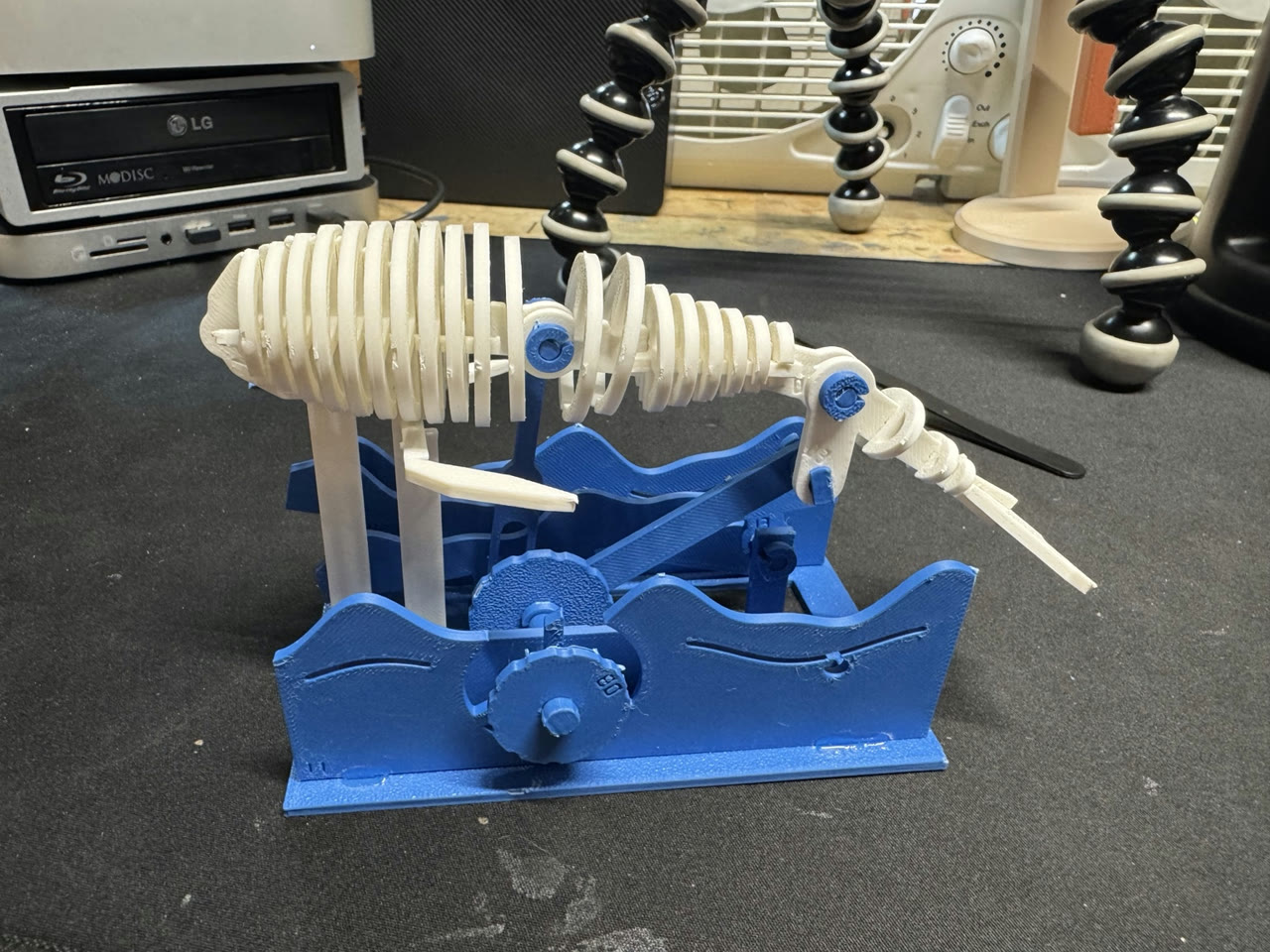 Assembled white mechanical whale with blue wave supports on Brian’s workbench