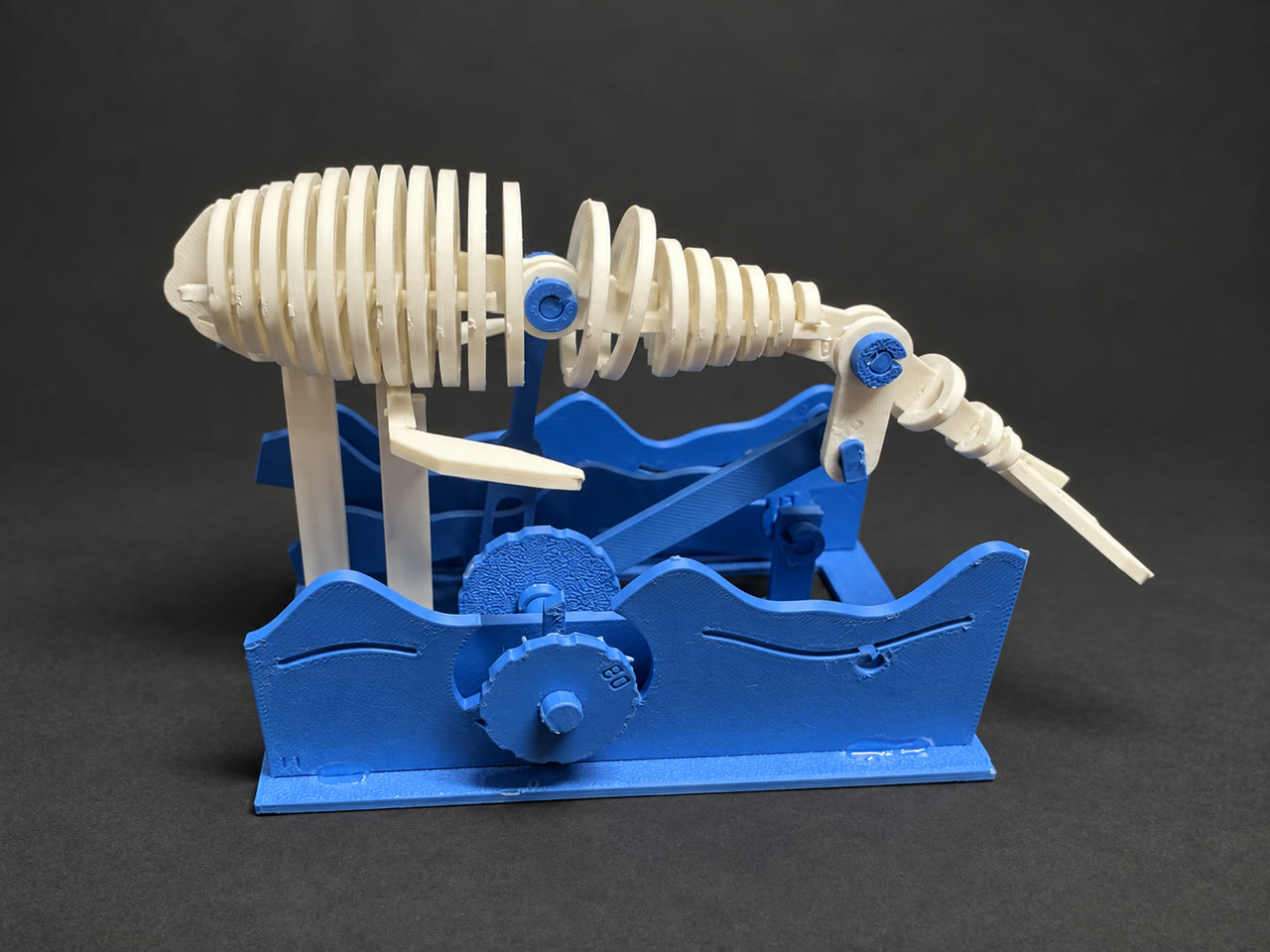 White v0.4.1 skeletal whale with blue wave supports and a hand crank on a cleaned charcoal background